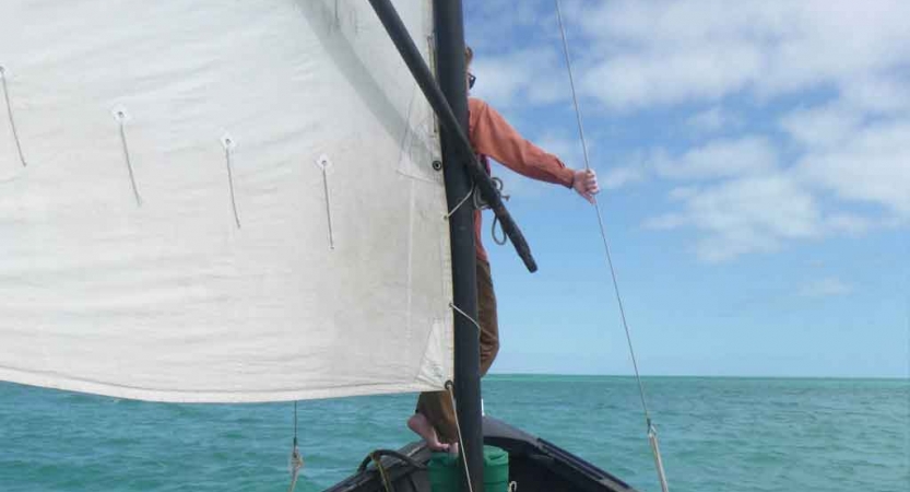 a person stands at the front of a sailboat holding a rope